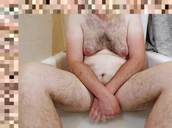 Obese or fat hairy man sitting naked in the bathtub soaking his butt while covering front